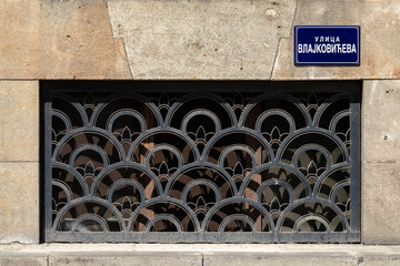 Cast lattice on a window in a stone wall. There is a plaque on the wall with the name of the...