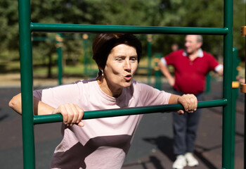 Fototapeta premium Mature woman doing push-ups from the crossbar on outdoor sports ground