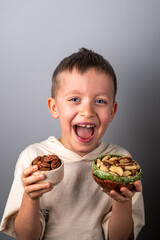 Cheerful little boy chooses between different nuts. Peeled pecan and Brazil nut. Healthy Eating.