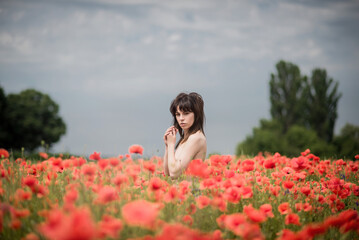 Fototapeta na wymiar A girl with black hair and bare shoulders poses in a poppy field.
