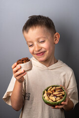 Cheerful little boy chooses between different nuts. Peeled pecan and Brazil nut. Healthy Eating.