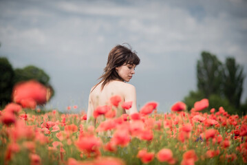 Fototapeta na wymiar A girl with black hair and bare shoulders poses in a poppy field.
