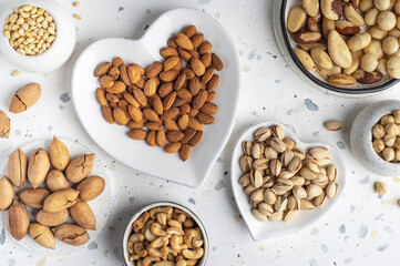 Different types of nuts on a plate in the shape of a heart. Assorted nuts on a white background. Top view.