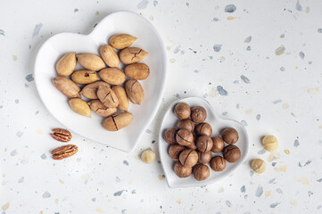 Pecan and macadamia in the shell in heart-shaped plates. Top view. Place for text