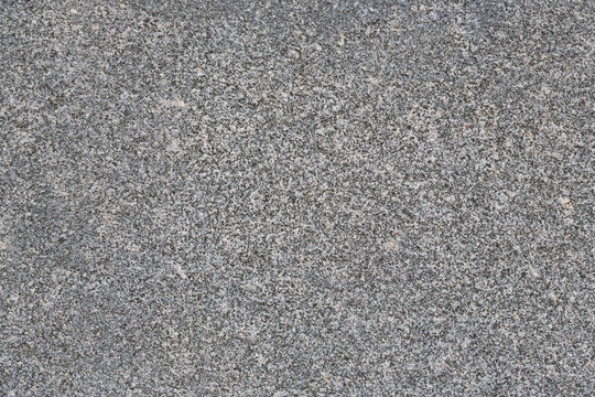 Granite texture. Natural gray granite with a grainy pattern. Stone background. Solid rough surface of rock. Durable construction and decoration material. Close-up.