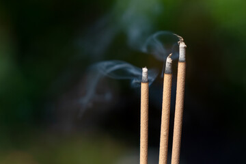 Three incense sticks burning with white smoke on dark brown background, Worship Worship in Asian beliefs and faith