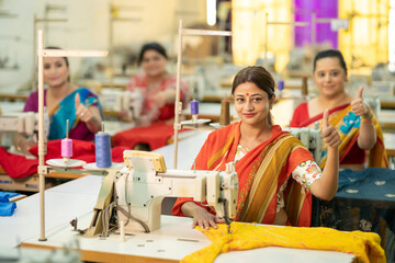 Indian women group showing thumbs up while work on sewing machine at textile factory.