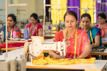 Indian women group working on sewing machine at textile factory.