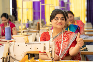 Indian women group showing thumbs up while work on sewing machine at textile factory.