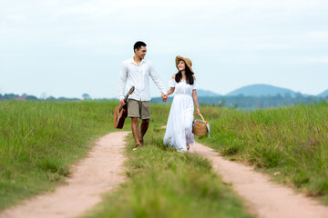 Lifestyle couple happy honeymoon in sunny time. Asian young couple sitting picnic and relax in the meadow in holiday. Romantic and In love. Lifestyle and Valentine concept
