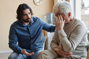 Portrait of male psychologist comforting senior man crying in mental health support group