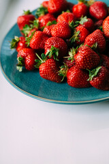 large ripe freshly picked strawberries in a ceramic plate on a turquoise background, close up