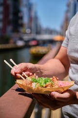 Unrecognizable man eating takoyaki at Dotonbori canal in Osaka, Japan.