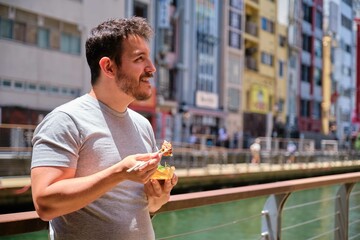 Obraz premium Tourist eating takoyaki at Dotonbori canal in Osaka, Japan.