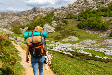 unrecognizable white woman equipped with backpack, sleeping bag and mat hiking in the mountains...