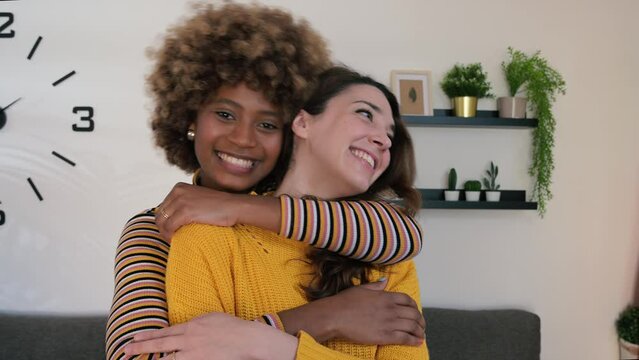 Beautiful and cheerful multiracial lesbian couple hugging at apartment. Two lovely and happy homosexual women embracing each other with their eyes closed at home.