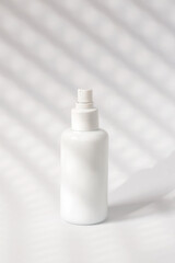 White cosmetic bottle on white background in sunlight, close up