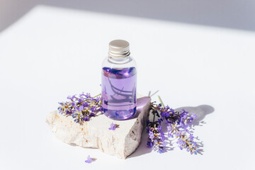 Lavender oil in transparent bottle on stone podium in sunlight. Natural cosmetics, aromatherapy concept. Closeup - obrazy, fototapety, plakaty