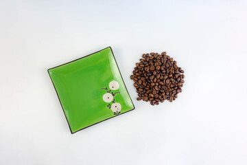 A pile of coffee beans next to a square green saucer, white background