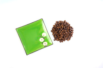 A pile of coffee beans next to a square green saucer, white background