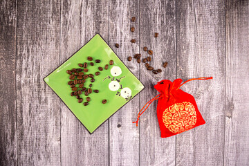 Coffee beans on a green saucer with a red bag next to it, wooden background, photo from above