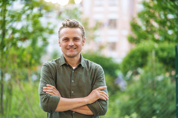 Blond, smiling, and handsome Caucasian man posing for camera in city park. Man's charming smile and...