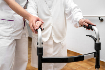 Nurse assists her senior patient on folding walker. Recuperation for elderly, seniors care, nursing...