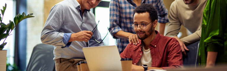 Group of happy multiracial business people looking at laptop screen, discussing project results and...