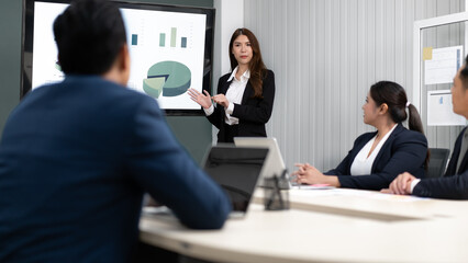 Fototapeta na wymiar Businesswoman standing in conference room giving statistic presentation. Young Asian professional business woman talking, presenting strategy planning to executive working team in corporate meeting.