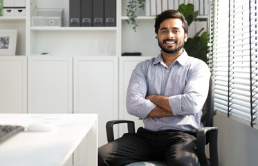 Portrait of indian businessman happy sitting arms crossed in modern office. Confident young smart bearded man entrepreneur looking at camera smiling. Friendly india ethnic manager work in workplace.