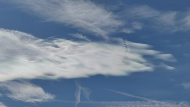 Natural blue sky background with Cloud iridescence, irisation around sun moving very slowly in shape of waves. Sunny autumn calm sky with colorful pearl colors - optical phenomenon in clouds.