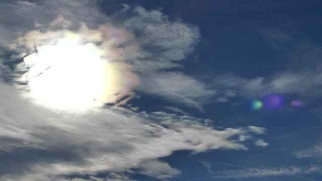 Natural blue sky background with white decorative clouds moving very slowly and Cloud iridescence, irisation around sun. Sunny autumn calm sky with colorful pearl colors - optical phenomenon in clouds