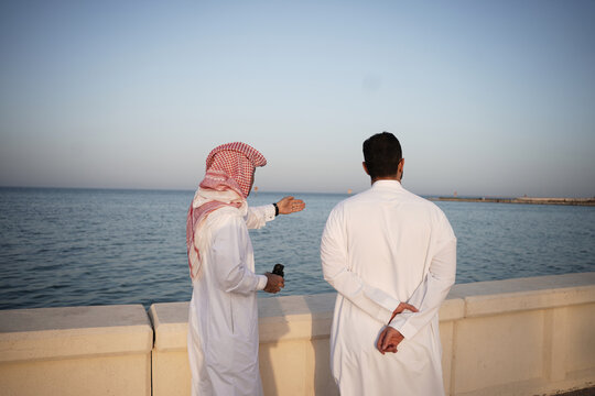Two Arabian men explore the world with a binocular. A man wearing thob and looking through the binocular on the sea.