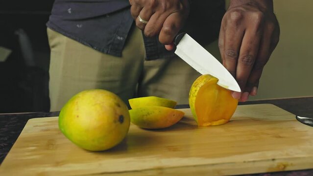 Closeup of male hands cutting mango fruit with a knife on a wooden board