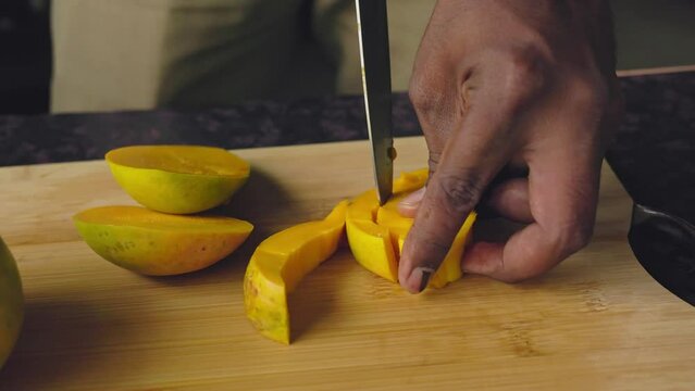 Closeup of male hands cutting mango fruit with a knife on a wooden board