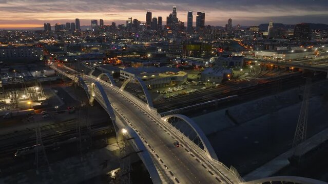 Fly Over Modern Road Bridge Spanning Water Canal And Railway At Dusk. Silhouettes Of Downtown Skyscrapers In Distance. Los Angeles, California, USA