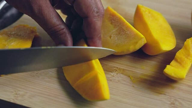 Closeup of male hands dicing a mango slice on a wooden chopping board