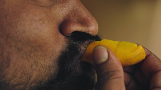 A bearded man savors the mango slice by enjoying it through sucking or eating