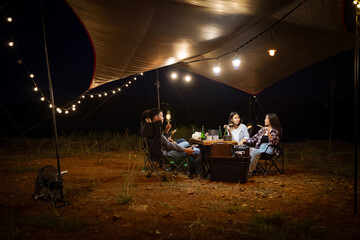 Young Asians eating barbecue under a canvas on a lake holiday evening having a tent under the lights.