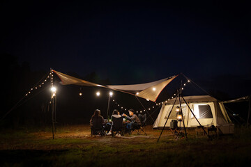 Young Asians eating barbecue under a canvas on a lake holiday evening having a tent under the lights.