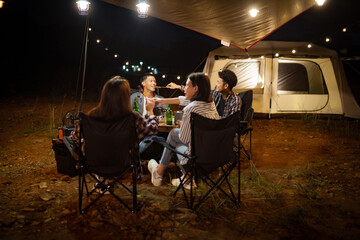 Young Asians eating barbecue under a canvas on a lake holiday evening having a tent under the lights.