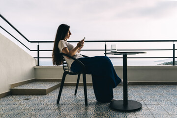 Woman sits with phone on balcony with beautiful view.