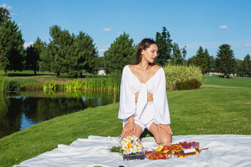 Young smiling woman relaxing outdoors and having a picnic, she is sitting on a blanket on the grass