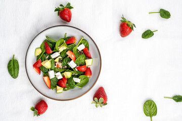 Summer fresh salad with strawberry, baby spinach, avocado and feta cheese in a plate on white background. Concept of health food.