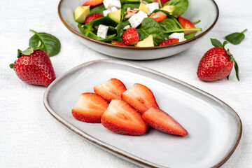 Summer fresh salad with strawberry, baby spinach, avocado and feta cheese in a plate on white background. Concept of health food.