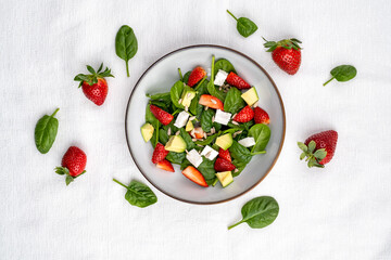 Summer fresh salad with strawberry, baby spinach, avocado and feta cheese in a plate on white background. Concept of health food.