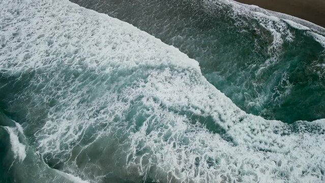 Foamy Waves Crashing In The Ocean Towards The Shore Of Caion In Spain. aerial tilt-up