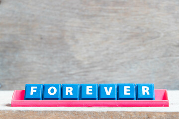 Tile alphabet letter with word forever in red color rack on wood background