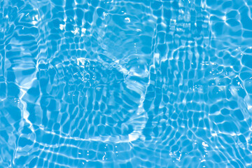 Blue water with ripples on the surface. Defocus blurred transparent blue colored clear calm water surface texture with splashes and bubbles. Water waves with shining pattern texture background.