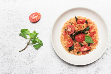 Tomato fried rice has basil in bowl on white slate table